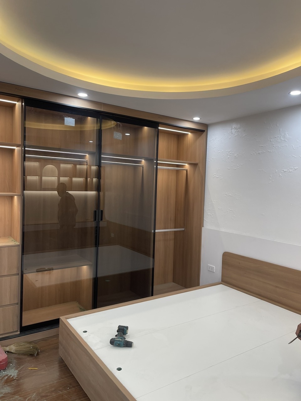 Phòng ngủ master với tủ áo cánh kính, giường ngủ và hệ đèn hắt